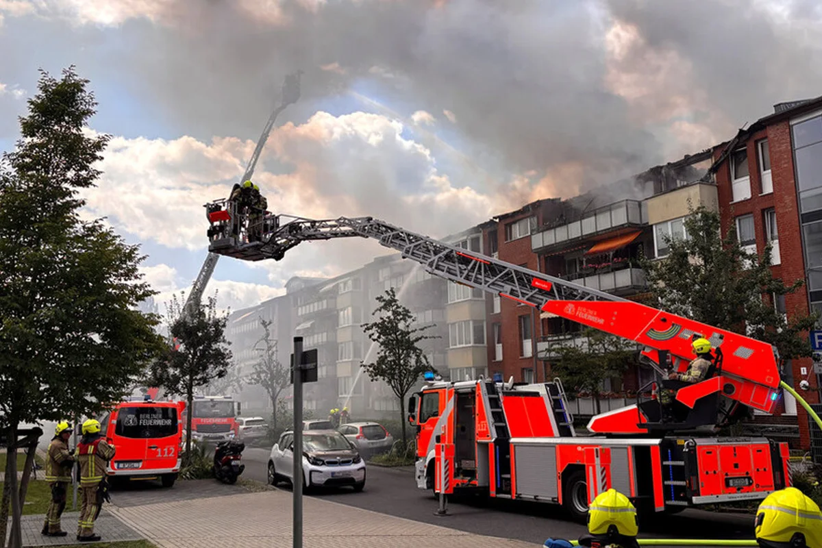 Feuerwehrleute stehen auf einer Drehleiter, um einen Brand in einem Mehrfamilienhaus zu löschen. Rauch steigt auf.