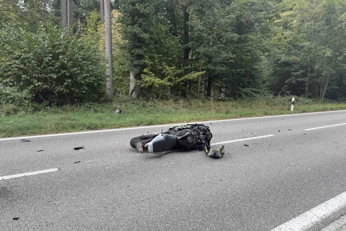 Ein umgestürztes Motorrad liegt auf einer Landstraße, umgeben von verstreuten Trümmerteilen, neben einem Waldstück.
