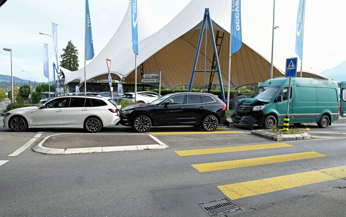 Drei Fahrzeuge stehen in einem Auffahrunfall direkt hintereinander auf einer Straße vor einem Gebäude mit Zeltüberdachung.