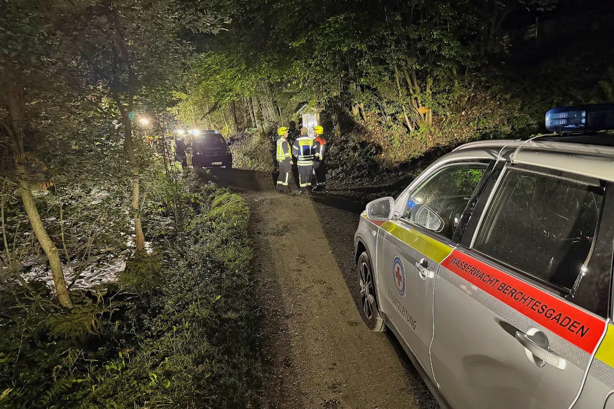 Ein Einsatzfahrzeug der Wasserwacht Berchtesgaden steht auf einem Waldweg, umgeben von Bäumen, mit Einsatzkräften, die sich in der Nacht absprechen.