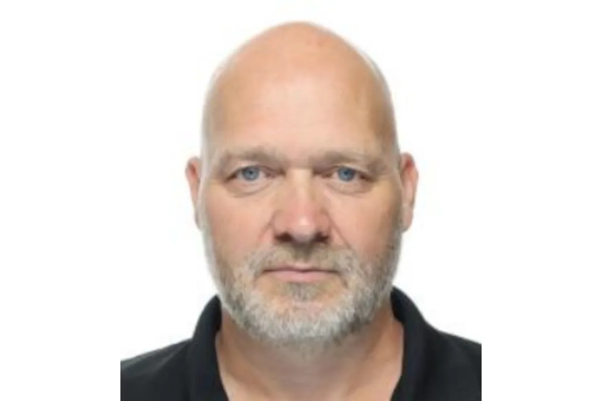 Das Bild zeigt das Porträt eines älteren Mannes mit Glatze und grauem Bart vor einem neutralen Hintergrund. Er trägt ein dunkles Oberteil und blickt direkt in die Kamera.