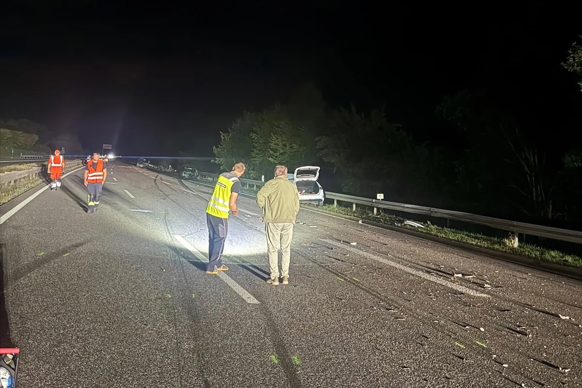 Mehrere Personen in orangefarbenen Sicherheitswesten laufen auf einer nächtlichen Autobahn. Ein Auto mit geöffnetem Kofferraum steht rechts.