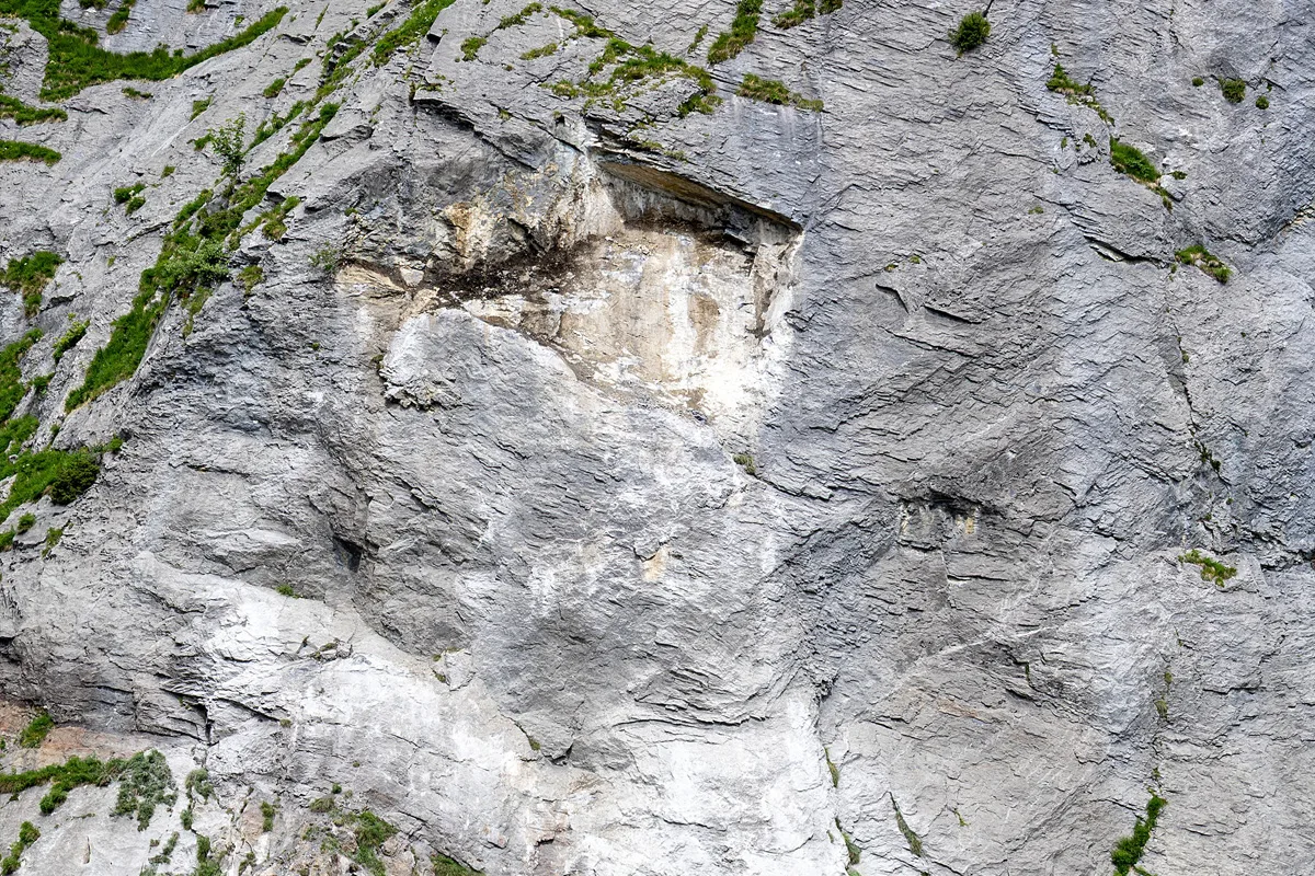 Die Aufnahme zeigt eine Felswand mit deutlichen Rissen, Abbrüchen und vereinzelter Vegetation an den Rändern. Der helle Stein hebt sich von der umgebenden Vegetation ab.