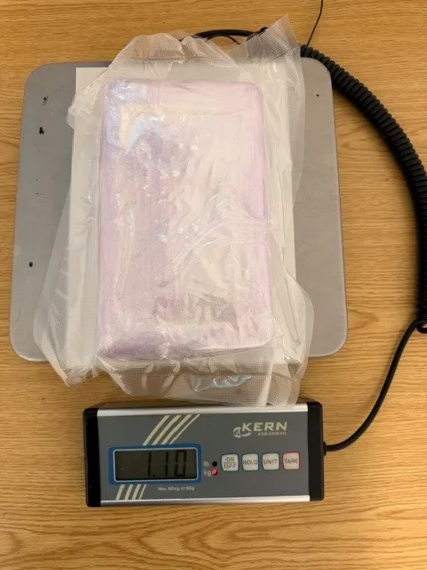 Ein rechteckiger, in Folie eingewickelter Block liegt auf einer digitalen Waage, die ein Gewicht von 1,1 kg anzeigt.