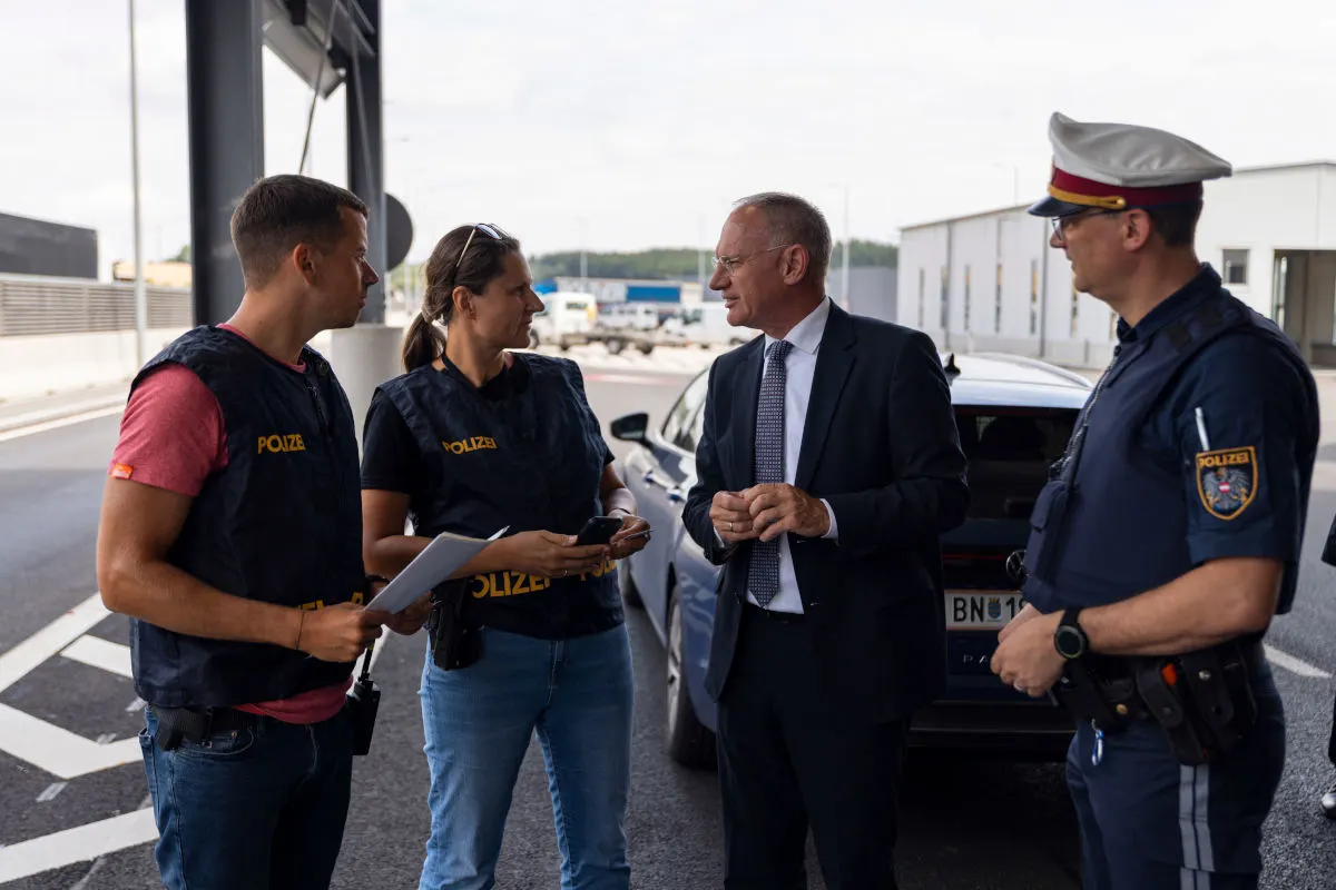 Drei Polizisten, von denen einer eine Uniform trägt, und eine Person im Anzug stehen auf einer Straße und reden miteinander. Ein Auto steht in der Nähe.