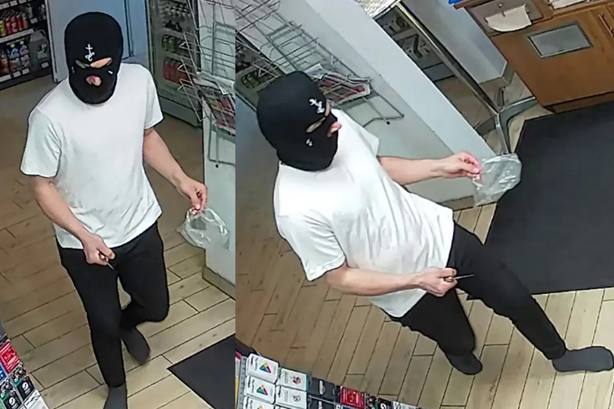 Eine Person in einer schwarzen Maske und weißem T-Shirt betritt mit einem Messer ein Geschäft. Der Boden ist aus Holz und es sind Regale im Hintergrund zu sehen.