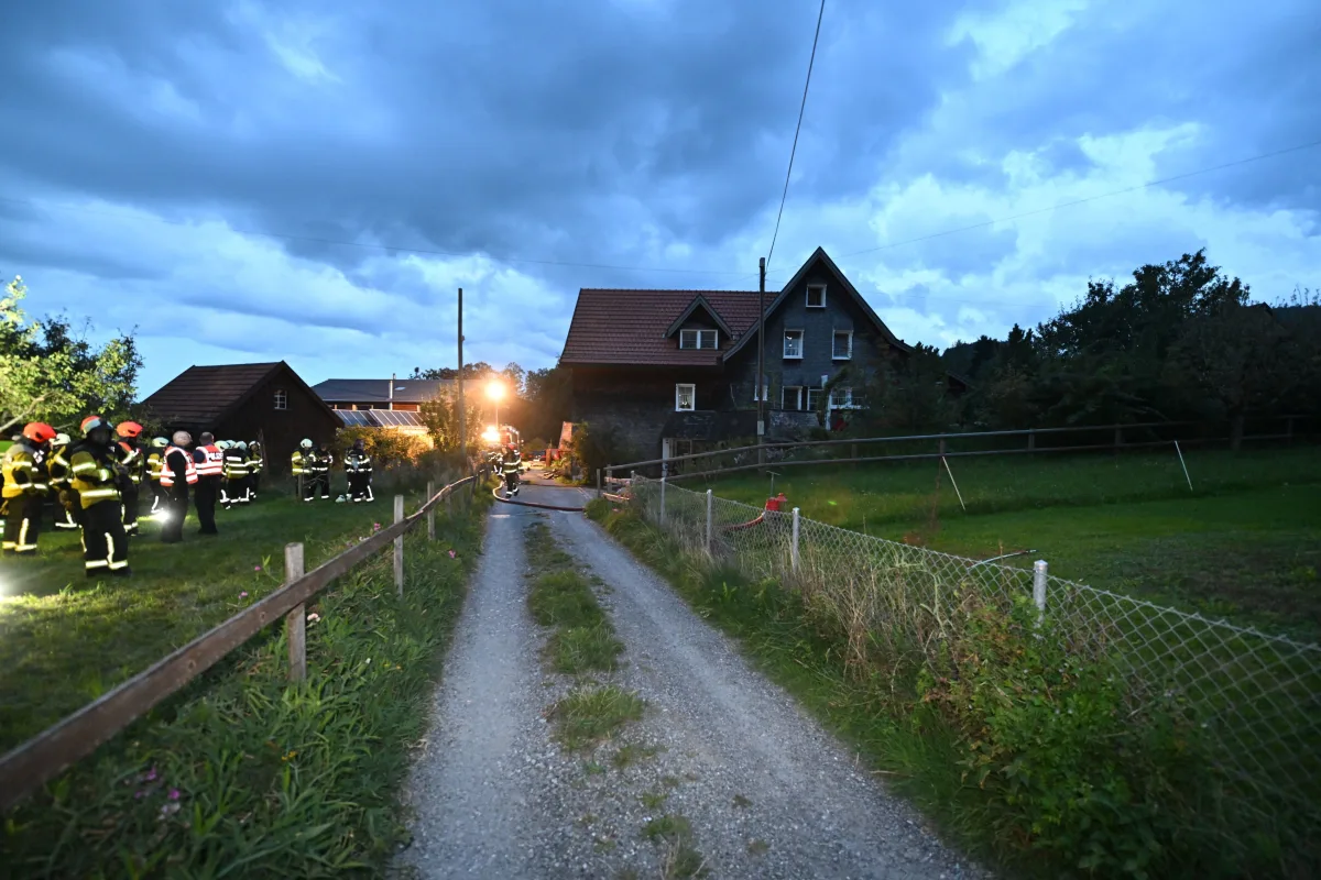 Feuerwehrleute in Einsatzkleidung stehen auf einem Feldweg vor einem Wohnhaus. Es ist Abenddämmerung.
