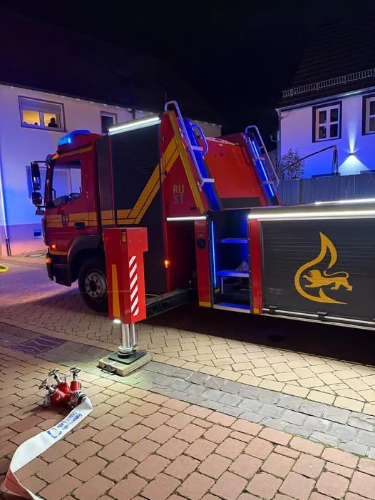 Ein Feuerwehrauto steht nachts mit eingeschaltetem Blaulicht in einer Wohnstraße, während ein Feuerlöscher am Boden liegt.