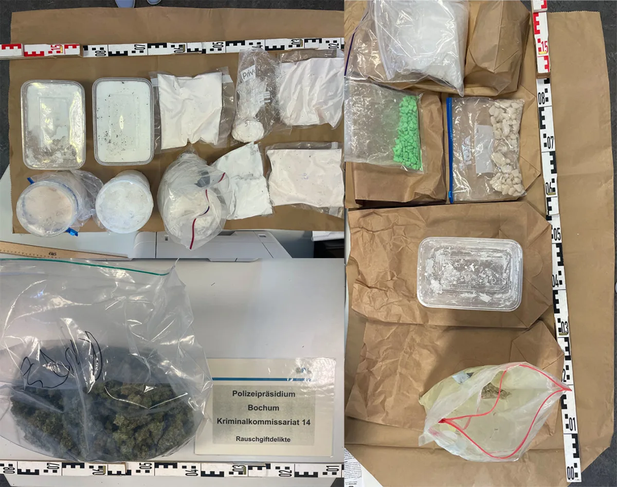 Eine Vielzahl von Drogen in verschiedenen Verpackungen liegt auf einem Tisch. Ein Schild des Polizeipräsidiums Bochum ist sichtbar.