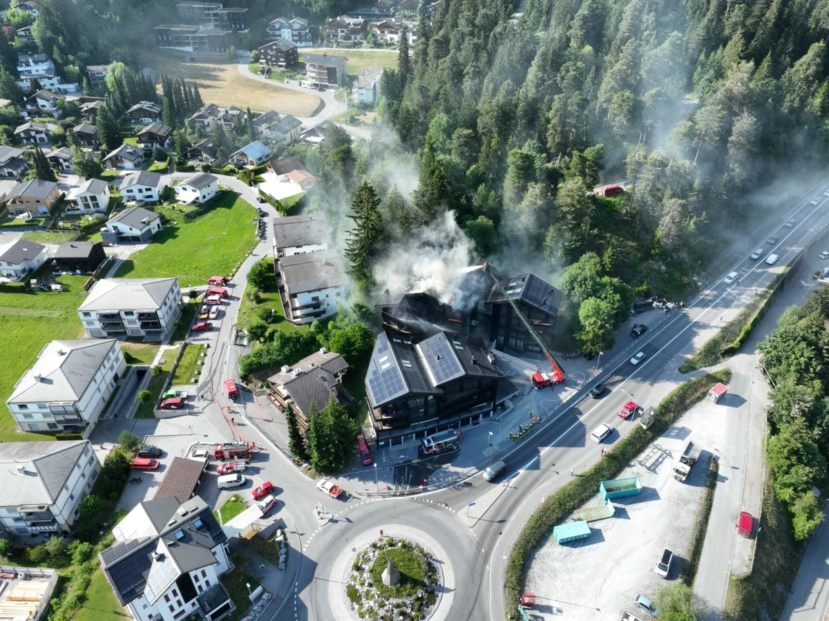 Von oben betrachtet ist in einem Dorf ein Gebäude zu sehen, aus dem dichter Rauch aufsteigt. Feuerwehrfahrzeuge sind vor Ort.