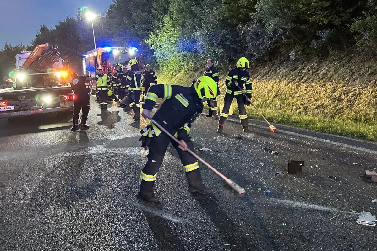 Feuerwehrleute in Schutzkleidung reinigen die Straße von Trümmern bei Nacht. Im Hintergrund stehen Einsatzfahrzeuge mit Blaulicht.
