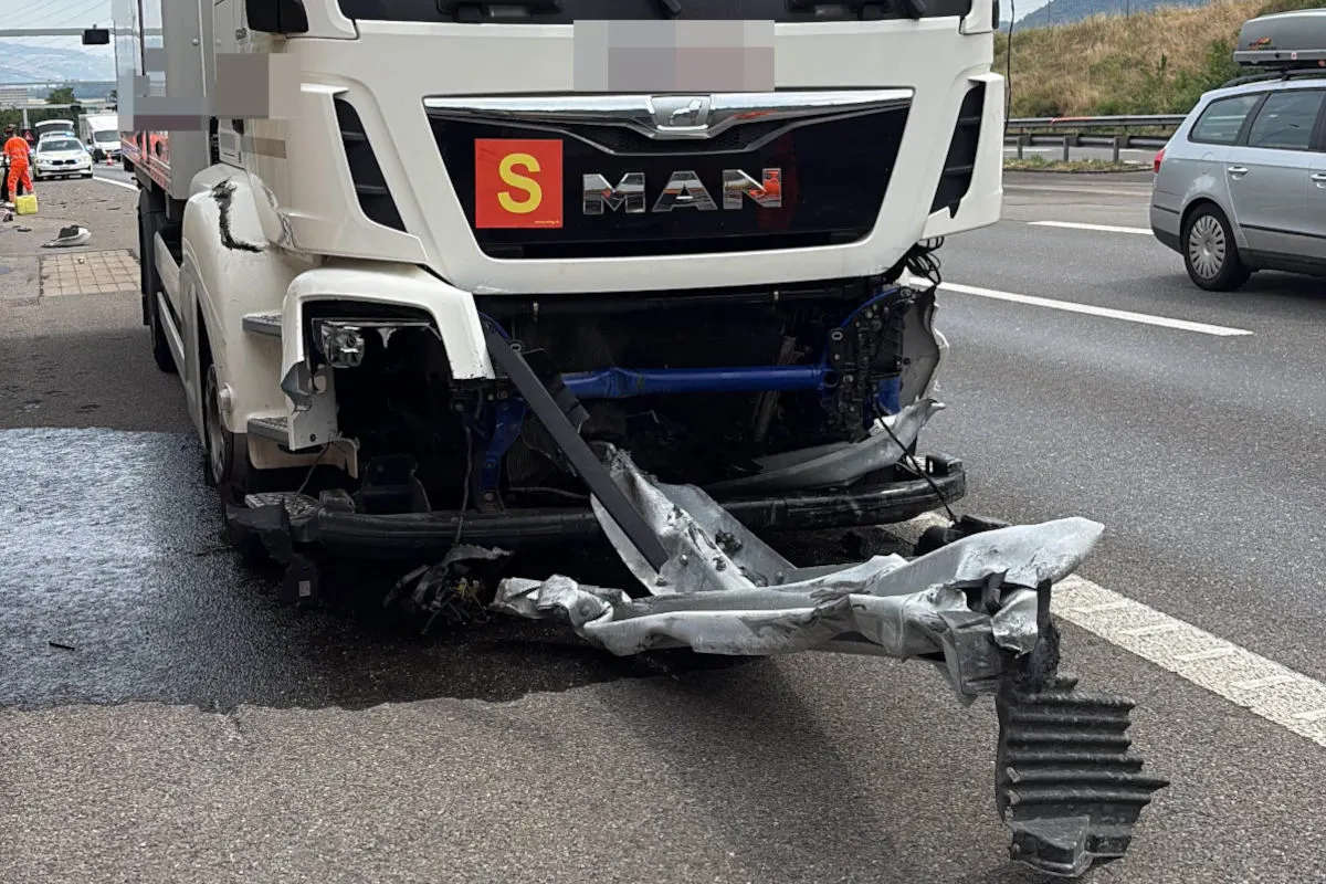 Ein weißer LKW mit stark beschädigter Front steht auf einer mehrspurigen Straße. Daneben sind weitere Fahrzeuge sichtbar.