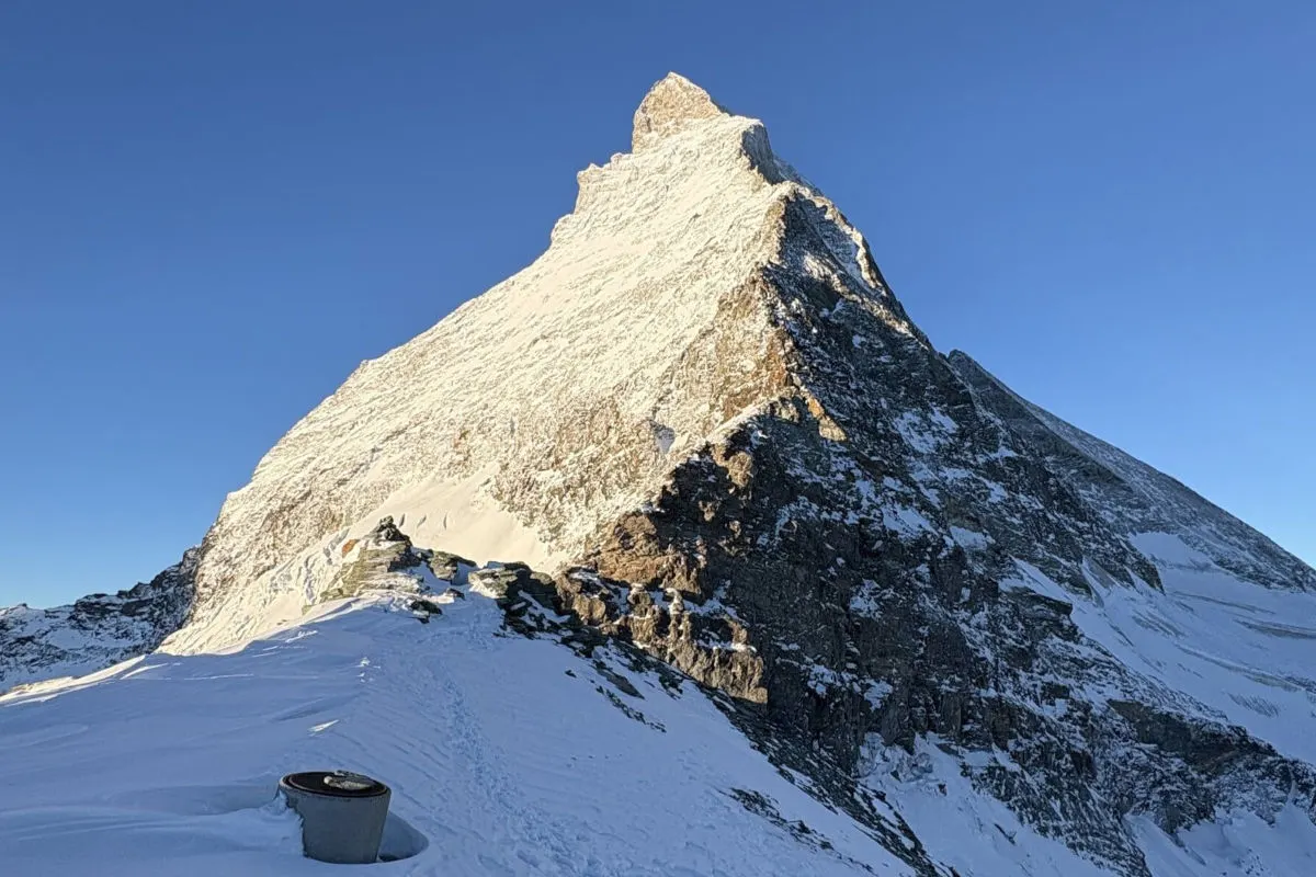 Das Bild zeigt das Matterhorn an einem klaren Tag, mit schneebedeckten Flächen und blauem Himmel im Hintergrund.