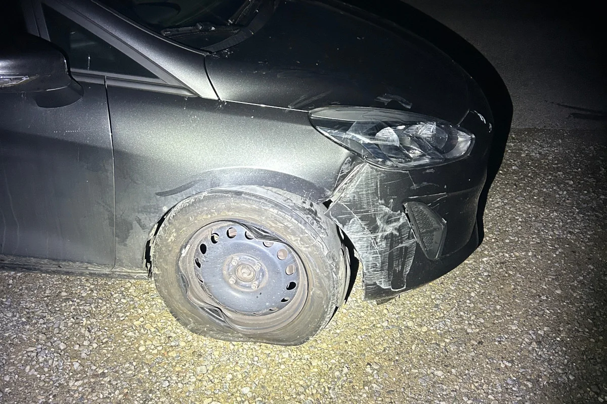 Das Bild zeigt das beschädigte Vorderrad eines dunklen Autos. Der Reifen ist platt und die Karosserie um das Rad herum ist verbeult.
