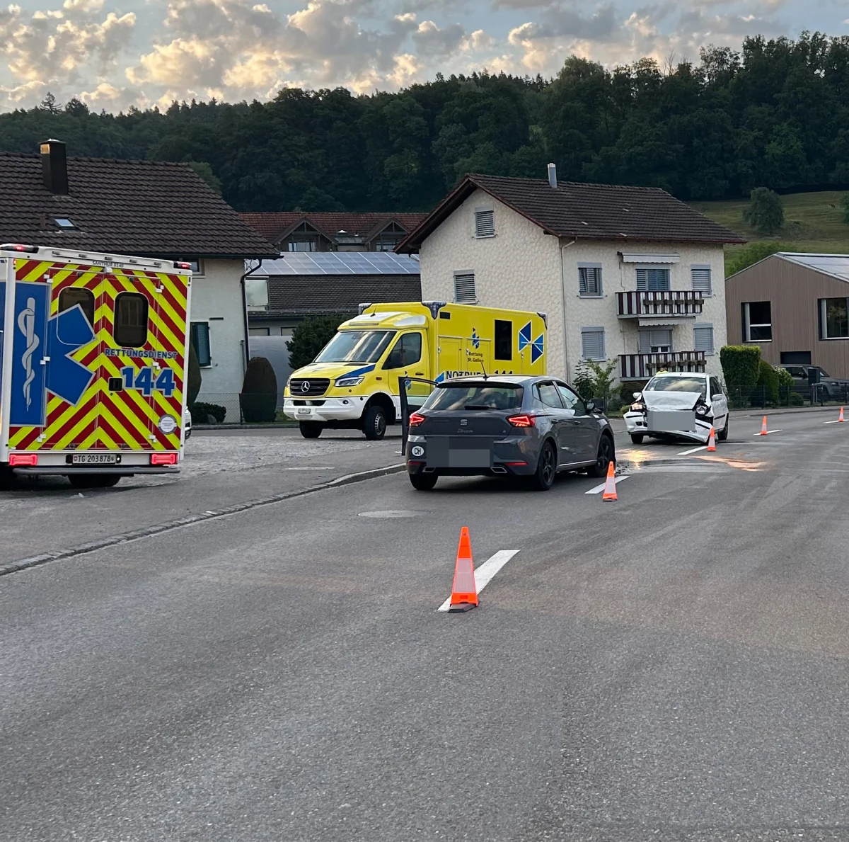Auf einer Straße in einem Wohngebiet stehen ein beschädigter weißer Pkw und zwei Krankenwagen. Der Pkw hat Frontschaden.