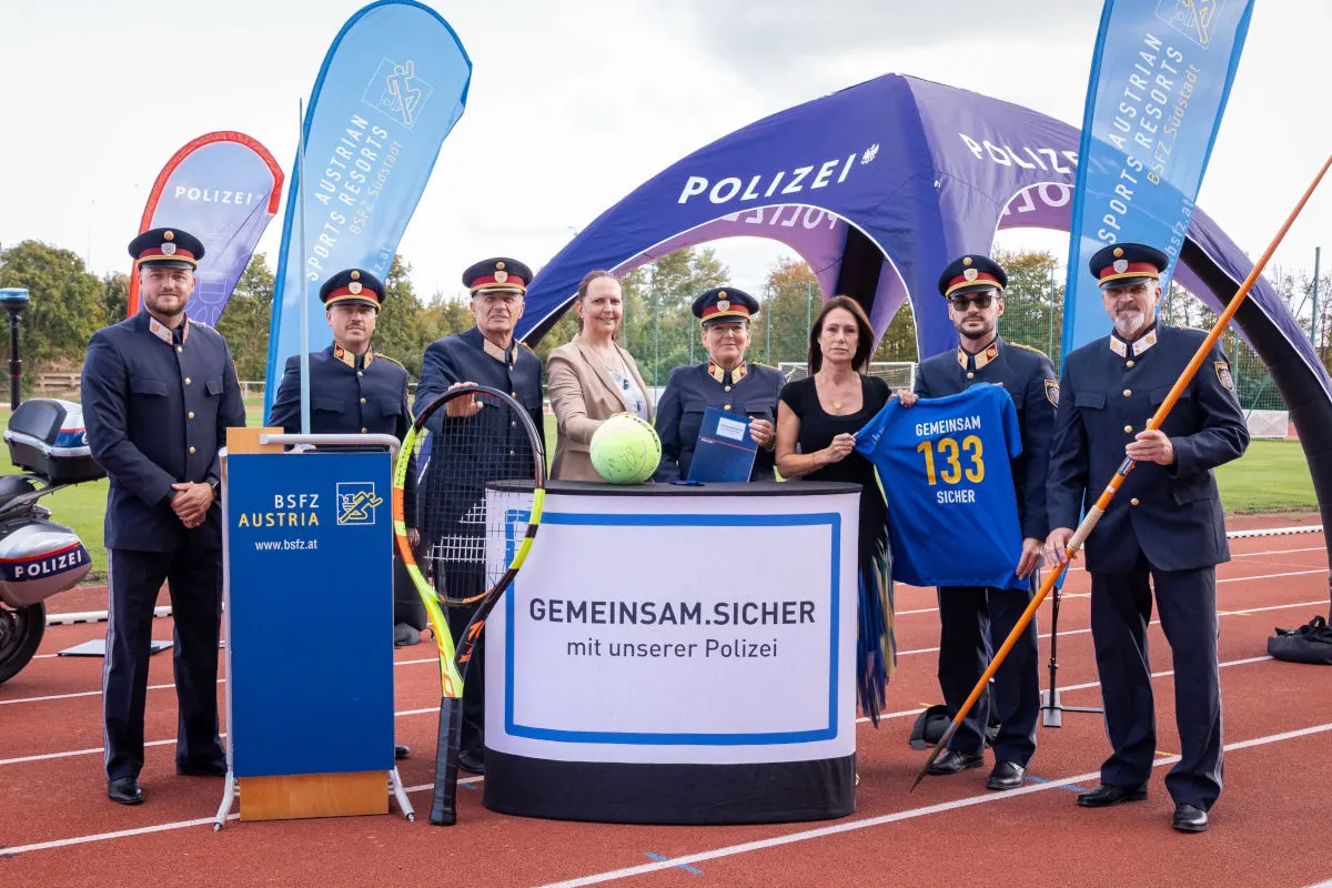 Mehrere uniformierte Personen stehen mit Sport- und Polizeiausrüstung auf einer Laufbahn. Ein Banner mit 'Gemeinsam.Sicher' ist sichtbar.