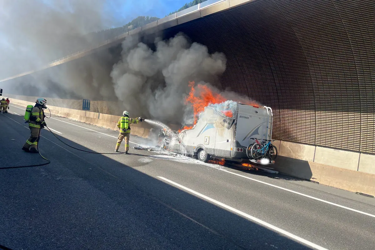 Ein Feuerwehrmann bekämpft die Flammen an einem brennenden Wohnmobil in einem Tunnel. Dichte Rauchwolken steigen auf.