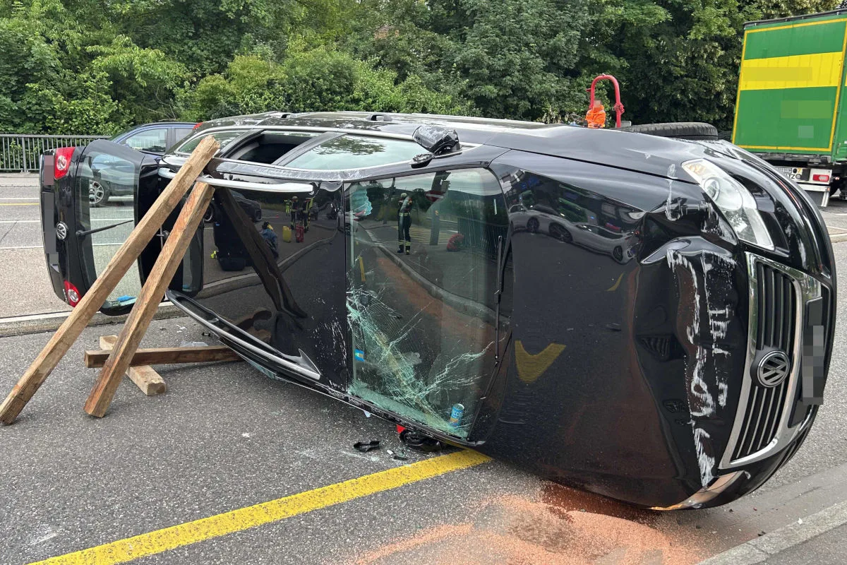 Ein schwarzer Pkw liegt nach einem Unfall auf der Seite. Die Scheibe ist beschädigt und das Fahrzeug wird durch Holzbalken gestützt.