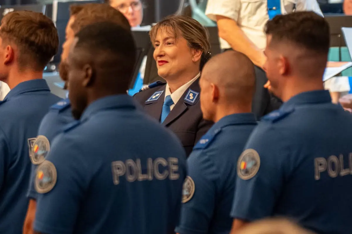 Mehrere Polizisten in blauen Uniformen, darunter eine Frau in der Mitte, nehmen an einer Zeremonie teil. Im Hintergrund sind weitere Personen zu sehen.