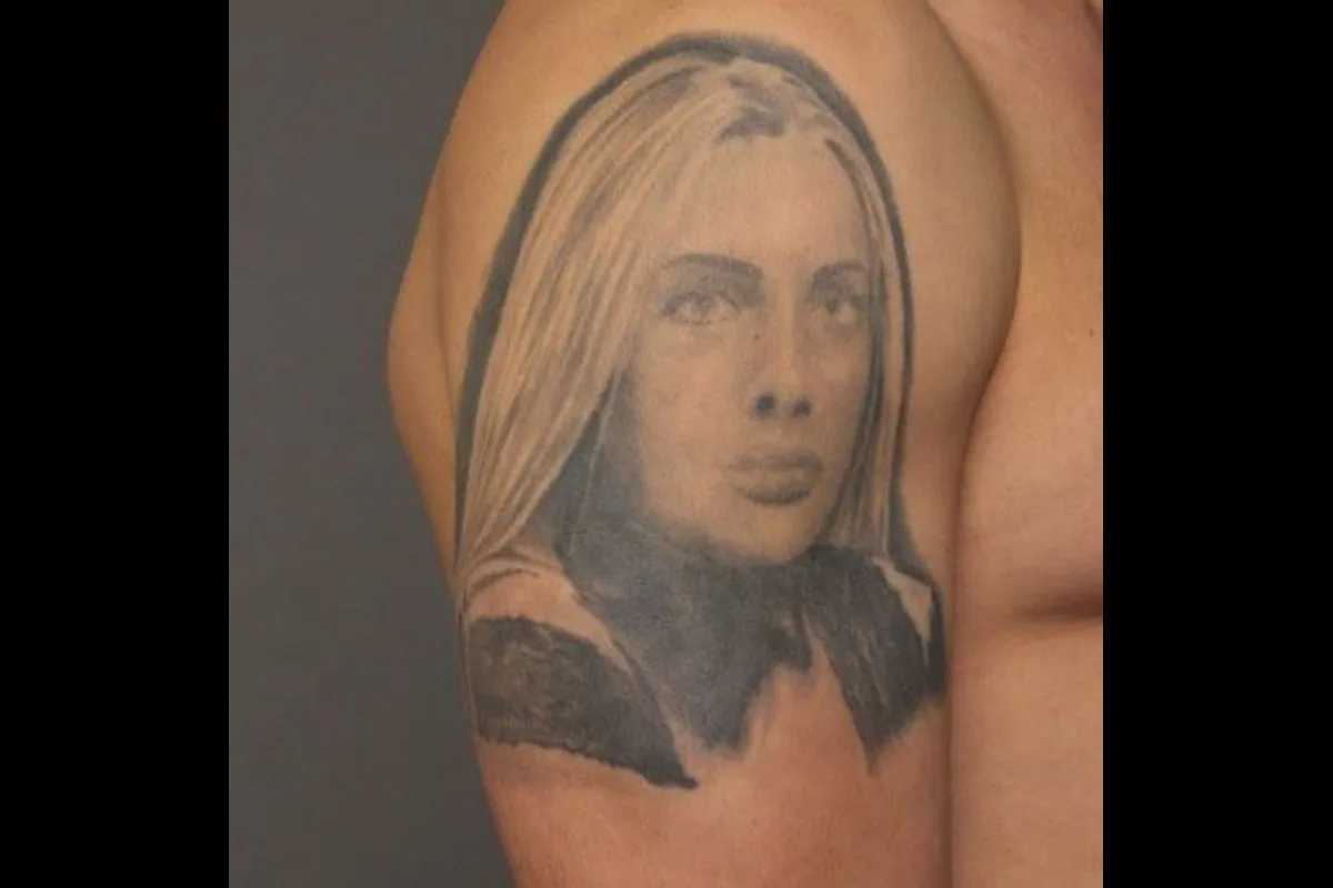 Ein Tattoo auf einem Oberarm zeigt das Gesicht einer Frau mit langen Haaren. Die Darstellung ist in Grautönen gehalten.