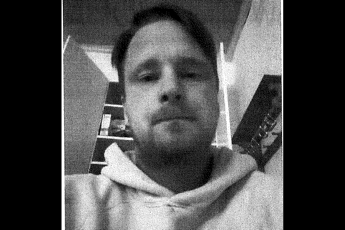 Ein unscharfes Schwarz-Weiß-Bild zeigt eine Person mit Bart und hellem Hoodie vor einem Regal im Innenraum.