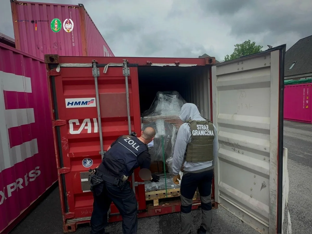 Zwei Uniformierte, einer vom Zoll und einer der Grenzpolizei, prüfen den Inhalt eines geöffneten Containers auf einem Terminalgelände.