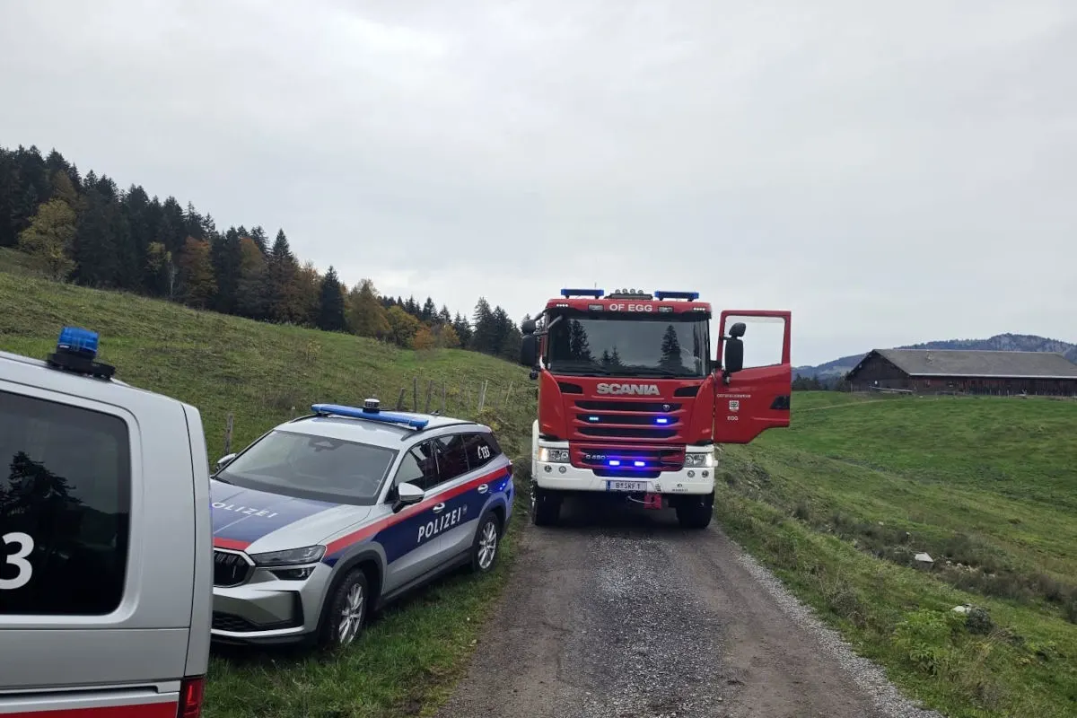 Ein Feuerwehrwagen der Marke Scania und ein Polizeiauto stehen auf einer schmalen Landstraße. Im Hintergrund sind Wälder und Hügel zu sehen.
