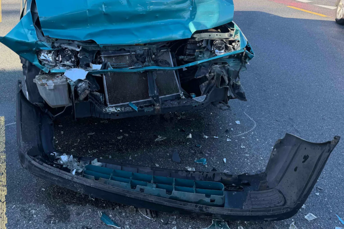 Die Front eines blauen Autos zeigt erhebliche Schäden nach einem Unfall. Teile der Stoßstange liegen auf dem Asphalt.