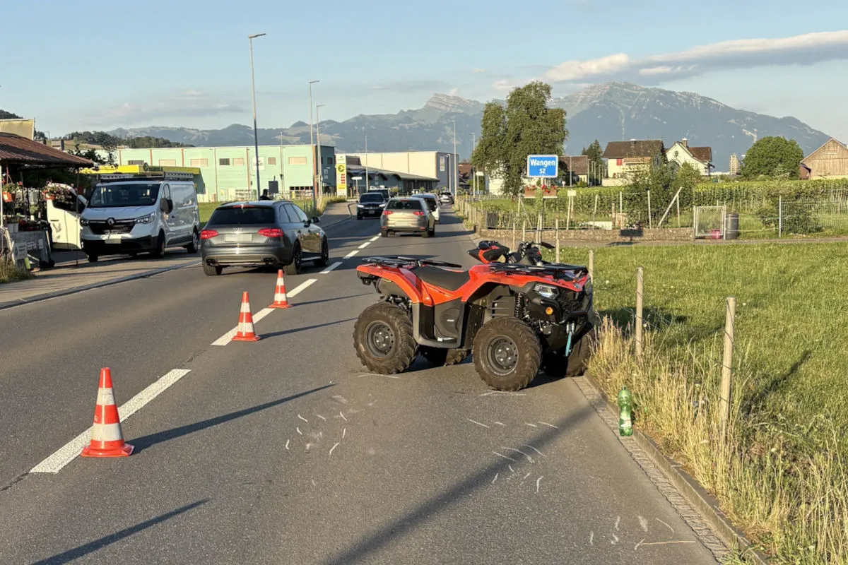Ein rotes Quad steht auf einer Fahrbahn in der Nähe von Wangen SZ, umgeben von einigen Leitkegeln. Mehrere Fahrzeuge sind auf der Straße zu sehen und im Hintergrund sind Berge erkennbar.