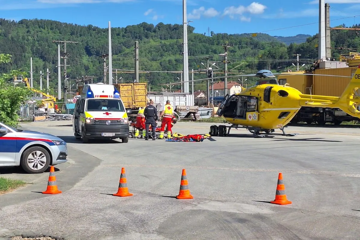 Ein Rettungshubschrauber und ein Krankenwagen stehen in einem offenen Bereich. Notfallpersonal ist um eine Person auf einer Trage versammelt.