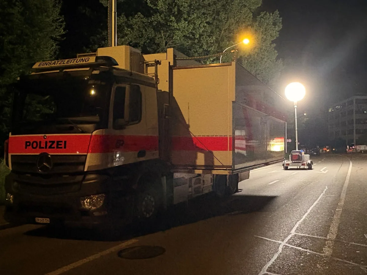 Ein Polizeifahrzeug mit der Aufschrift 'Einsatzleitung' steht nachts auf einer Straße. Ein heller Scheinwerfer leuchtet die Szene aus.