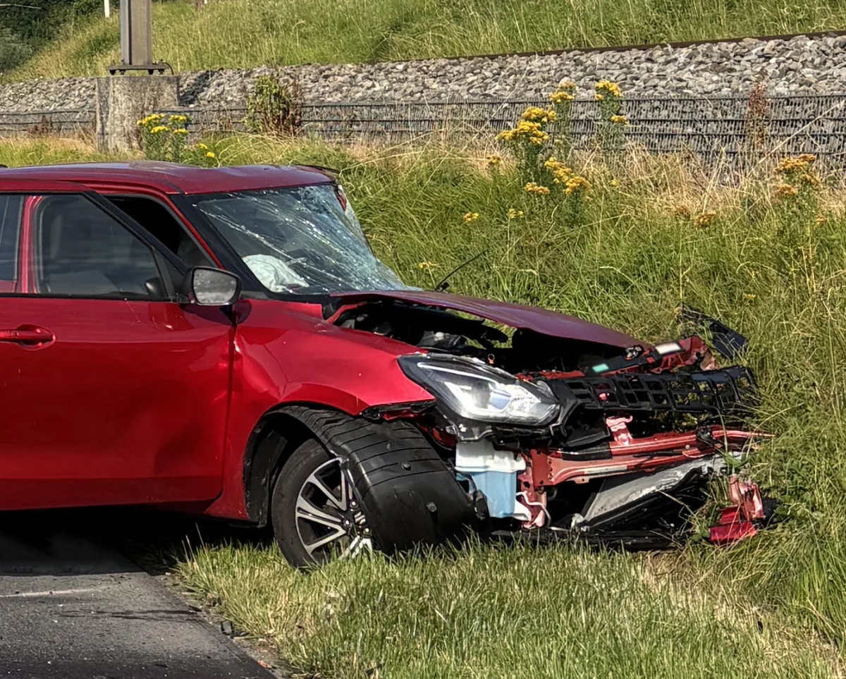 Ein rotes Auto ist stark beschädigt und steht neben einem Bahngleis. Die Frontpartie ist eingedrückt und der Kotflügel verformt.