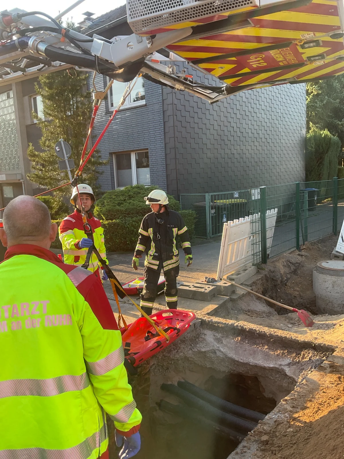Mehrere Einsatzkräfte der Feuerwehr und Rettungsdienste arbeiten an einer Baugrube, um eine Rettungsaktion durchzuführen.