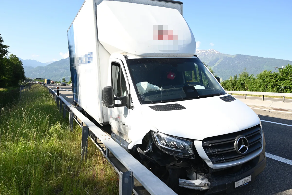 Ein weißer Mercedes-Lieferwagen mit sichtbaren Frontschäden steht auf der Autobahnleitplanke. Im Hintergrund sind Berge zu sehen.