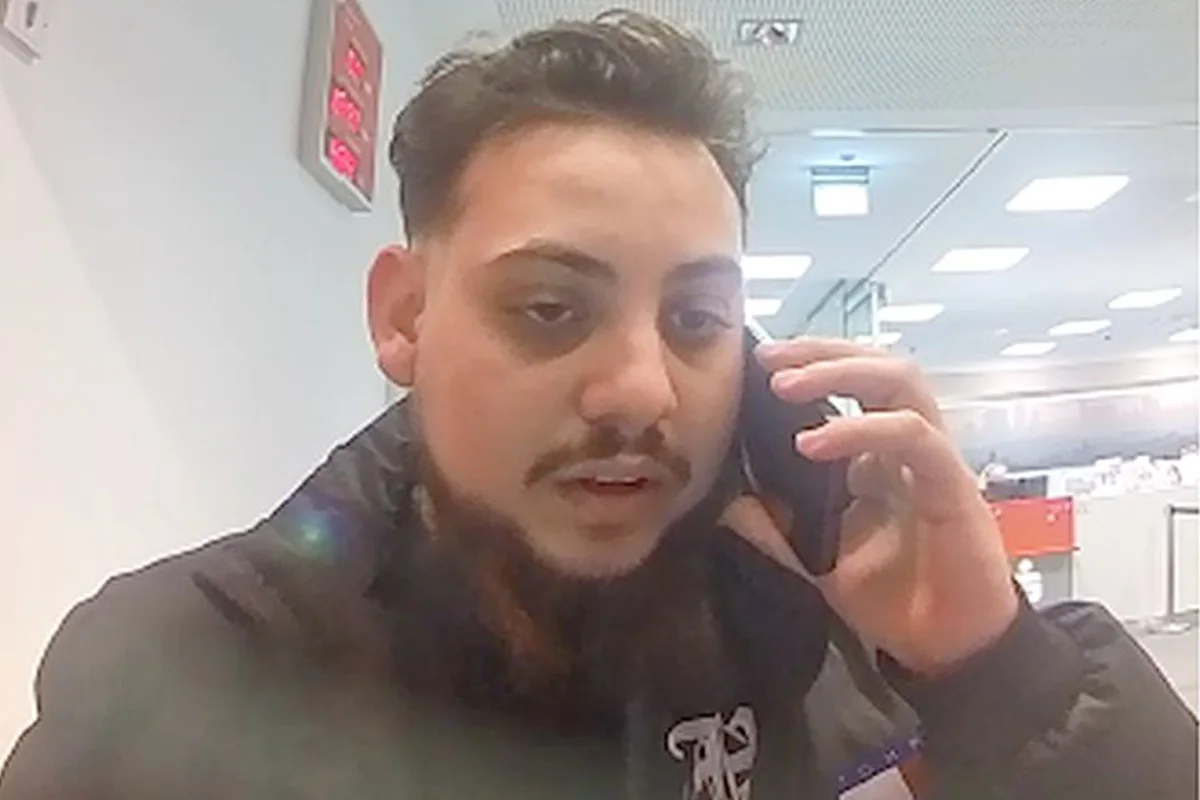 Ein Mann hält ein Handy ans Ohr und befindet sich in einem Bürogebäude mit weißen Deckenplatten und einem roten Schild.