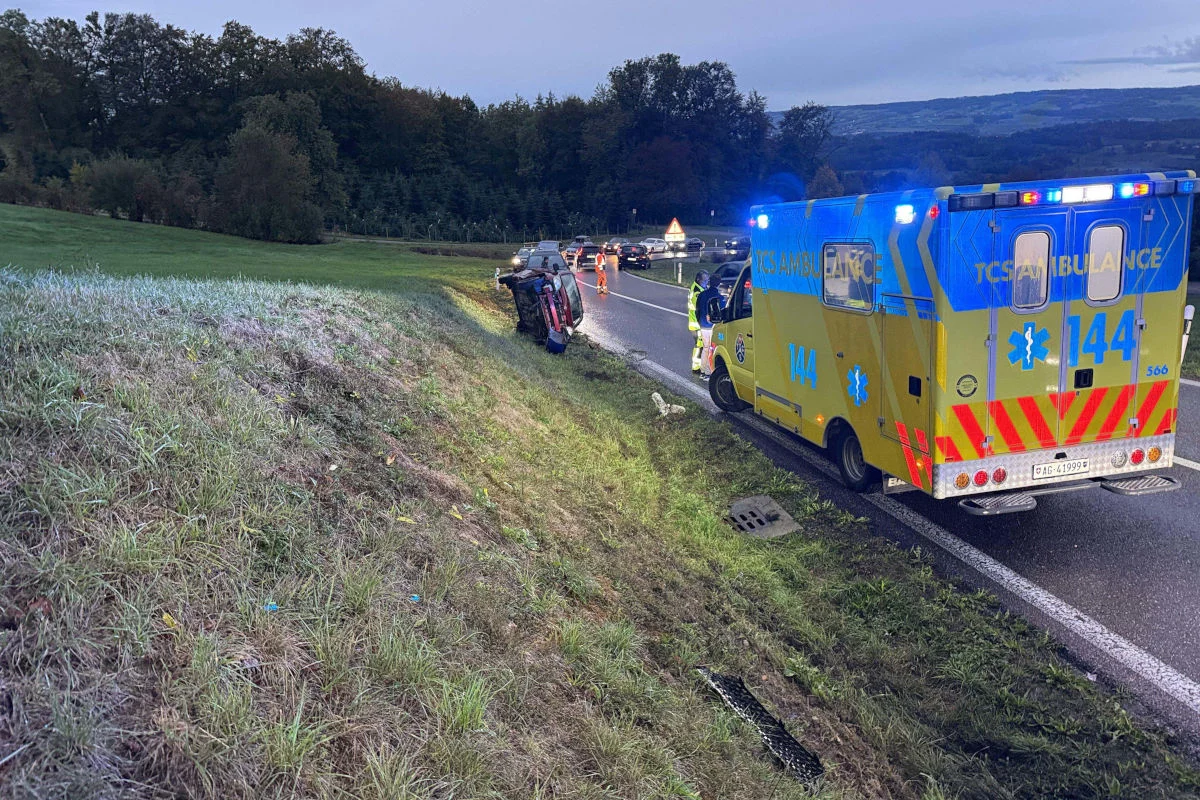 Ein Auto liegt an einer Böschung auf der Seite, während ein Rettungswagen daneben steht. Mehrere Personen befinden sich vor Ort.