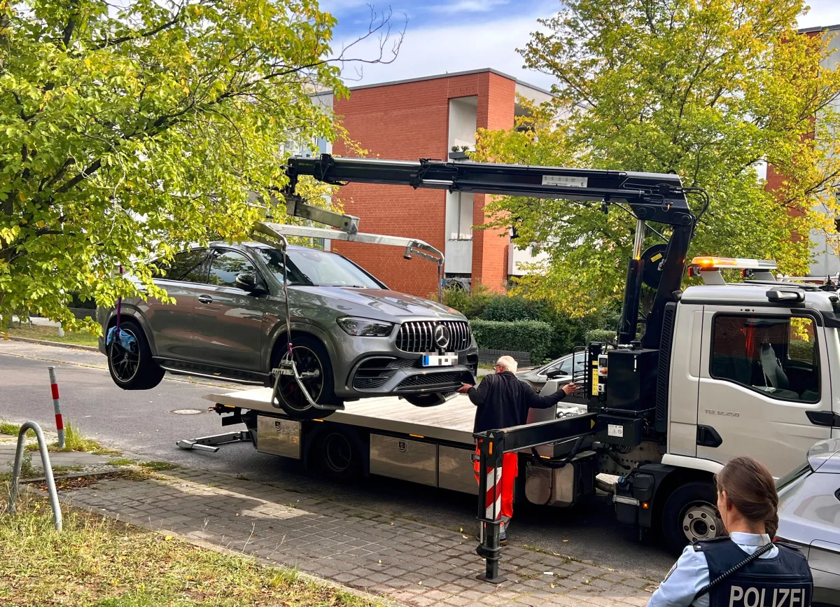 Ein silberner Mercedes wird von einem Kran auf einen Abschleppwagen gehoben. Im Vordergrund steht eine Person mit Polizeiaufschrift am Ärmel.