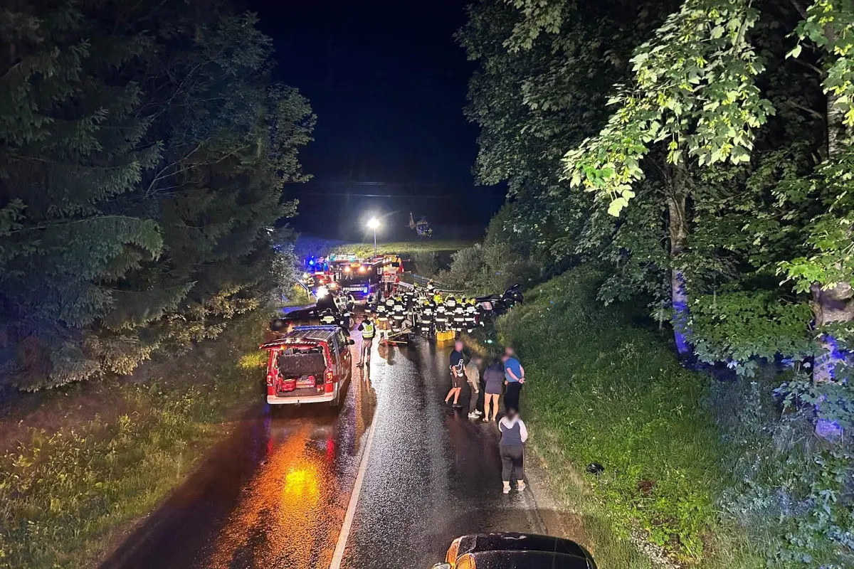 Eine nächtliche Szene auf einer Landstraße zeigt Einsatzkräfte und Fahrzeuge. Ein Hubschrauber ist im Hintergrund sichtbar.