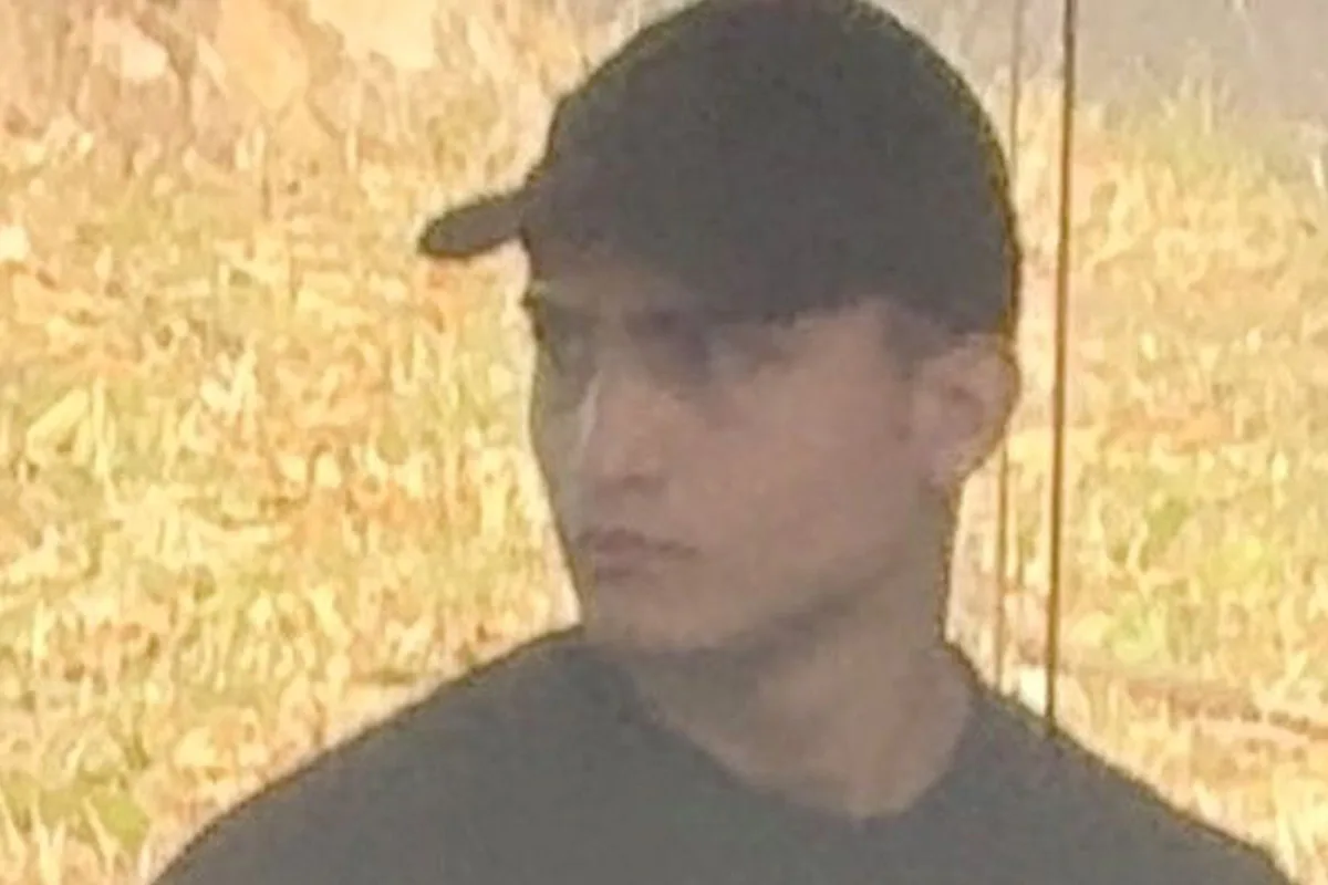 Eine Person mit schwarzem T-Shirt und Kappe ist in einem Freien zu sehen und schaut zur Seite. Der Hintergrund ist unscharf und zeigt wahrscheinlich Vegetation.