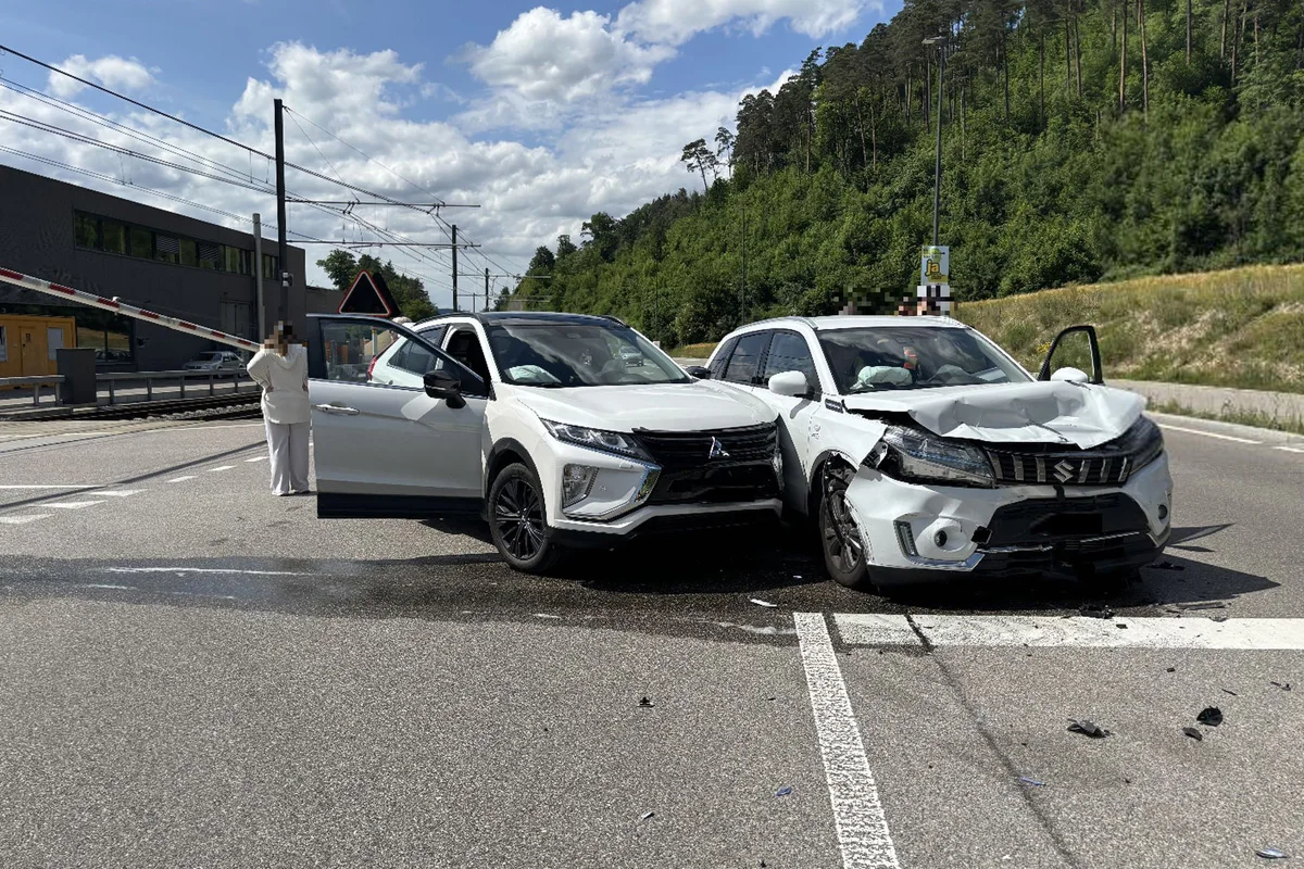 Zwei weiße SUVs stehen beschädigt auf einer Straße neben einem Bahnübergang. Eine Person steht neben einem der Fahrzeuge.