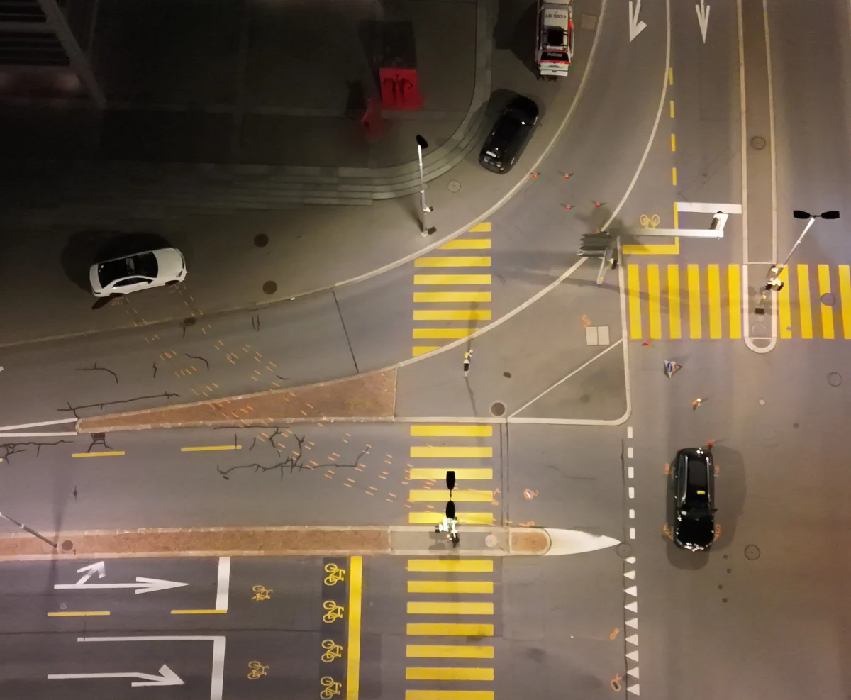 Luftbild zeigt eine Kreuzung bei Nacht mit mehreren Fahrzeugen und deutlichen Fahrbahnmarkierungen sowie Verkehrsschildern.