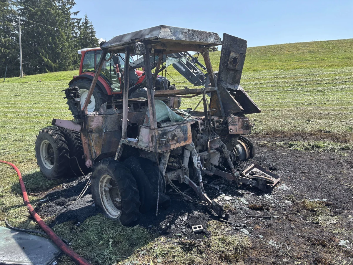 Ein Traktor ist vollständig ausgebrannt und steht auf einem Feld. Der Boden um den Traktor ist verbrannt und verkohlt.