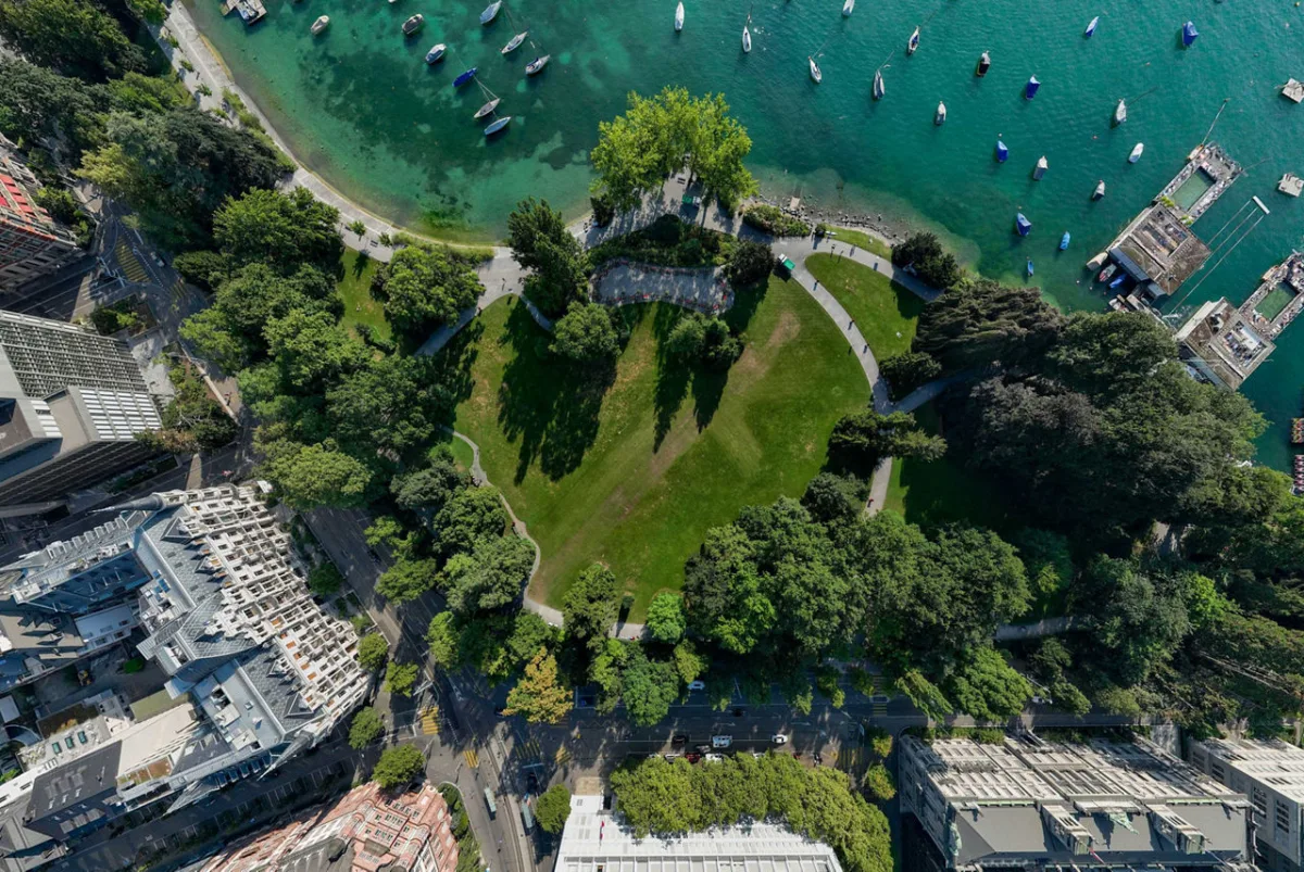 Eine Luftaufnahme zeigt einen grünen Park am Ufer eines Sees, umgeben von Gebäuden und vielen geparkten Booten im Wasser.