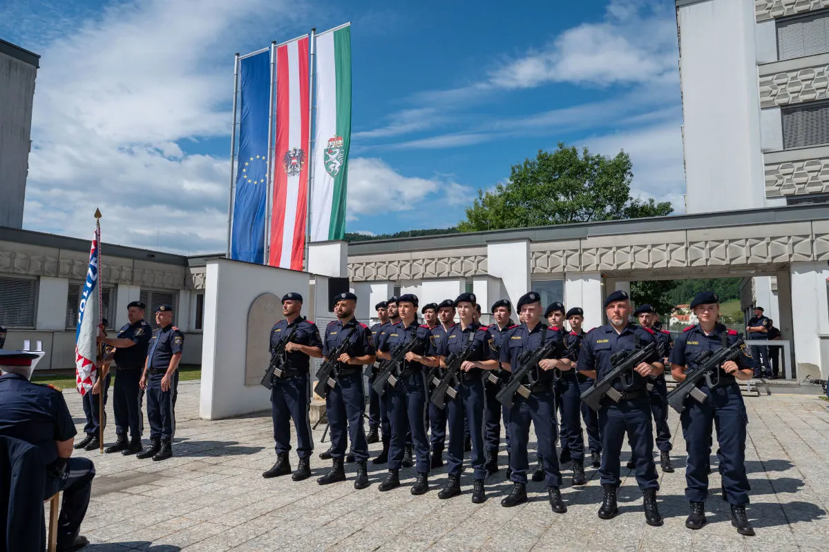 Eine Gruppe von uniformierten Polizisten steht stramm in einer Reihe unter Flaggen. Der Himmel ist klar und die Umgebung ist urban.