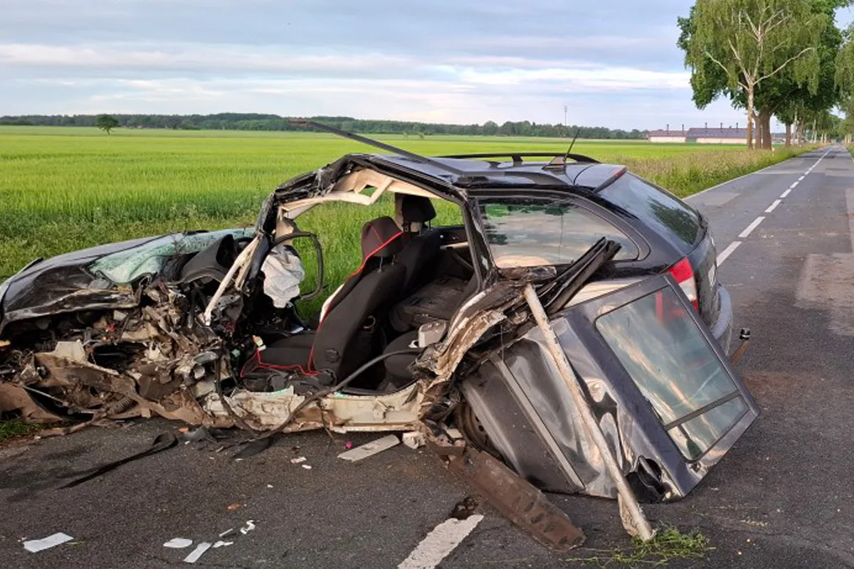 Ein Auto mit starkem Schaden an der Seite steht auf einer Landstraße. Die Umgebung ist ländlich mit grünen Feldern.