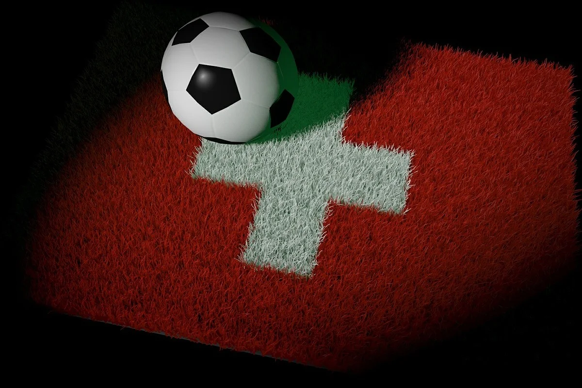 Ein Fußball liegt auf einer rot-weißen Oberfläche, die ein Schweizer Kreuz darstellt, möglicherweise symbolisch für Fußball in der Schweiz.