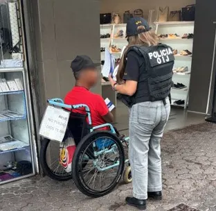 Eine Polizistin unterhält sich mit einem Mann im Rollstuhl auf dem Gehweg vor einem Geschäft.