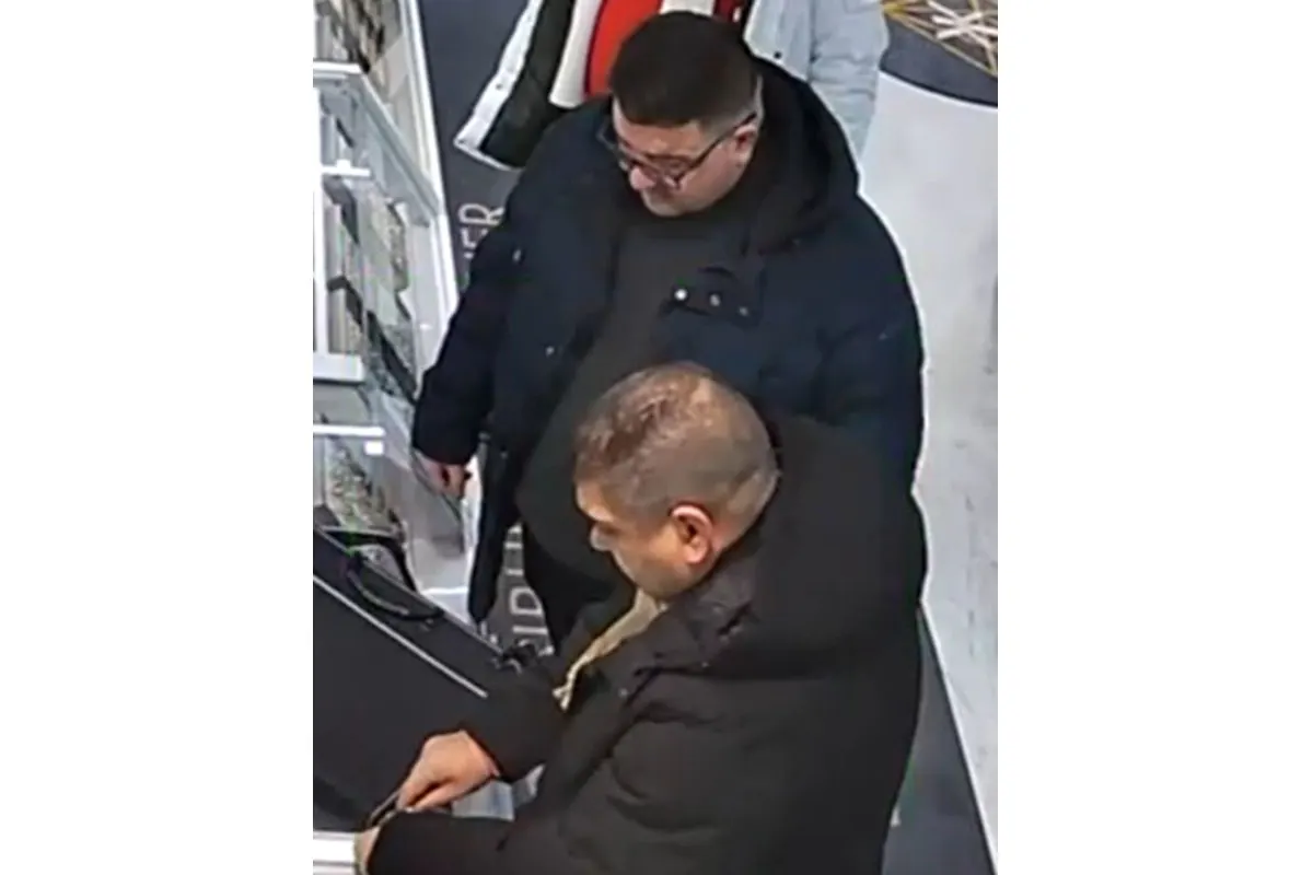 Zwei Männer in dunklen Jacken befinden sich in einem Geschäft, einer schaut auf ein Objekt, der andere steht daneben.