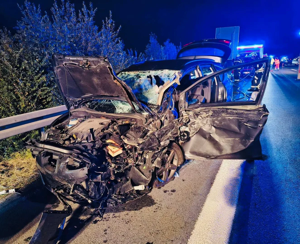 Ein zertrümmertes Auto steht mit offenen Türen an einer Leitplanke auf der Autobahn, umgeben von nächtlichem Blaulicht.
