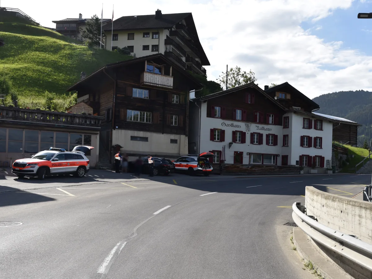 Drei Polizeifahrzeuge stehen vor einem Gasthaus mit Holzfassade in einer bergigen Umgebung unter klarem Himmel.